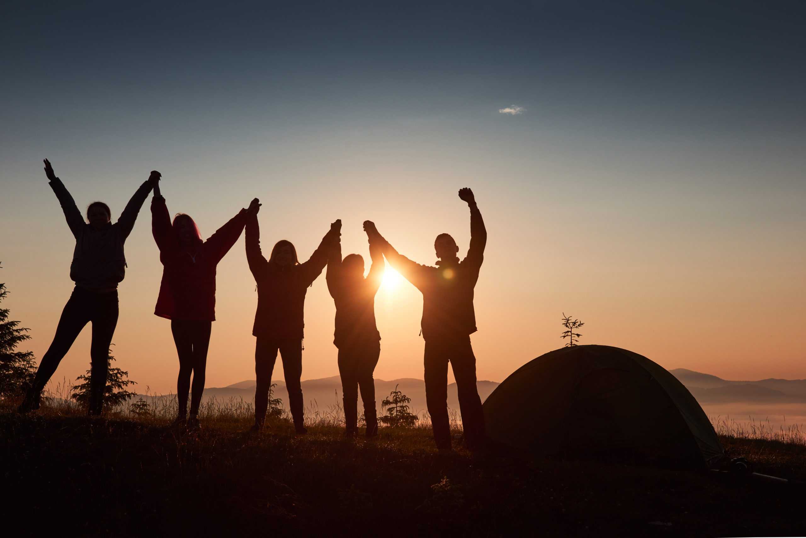 a-silhouette-of-group-people-have-fun-at-the-top-of-the-mountain-near-the-tent-during-the-sunset-scaled