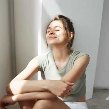 portrait-of-tender-young-beautiful-woman-smiling-with-closed-eyes-enjoying-morning-sunlights-sitting-on-floor-over-white-wall-1-350x350